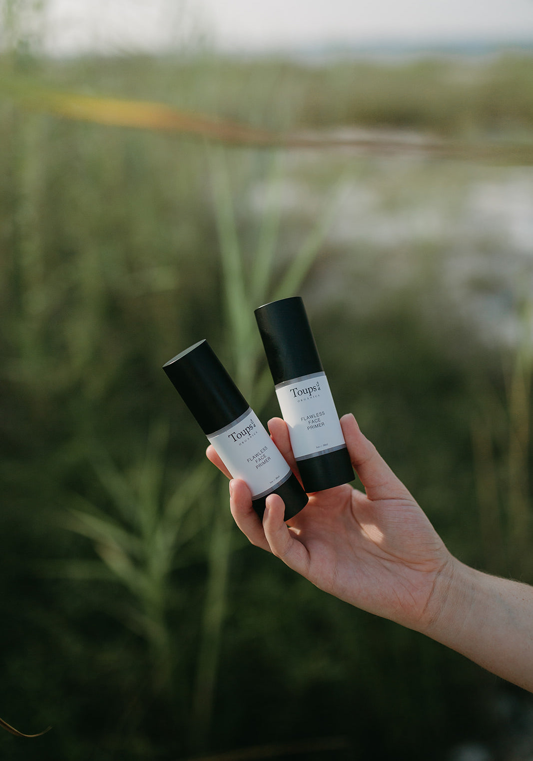 woman-holding-two-makeup-primers-against-beach-background