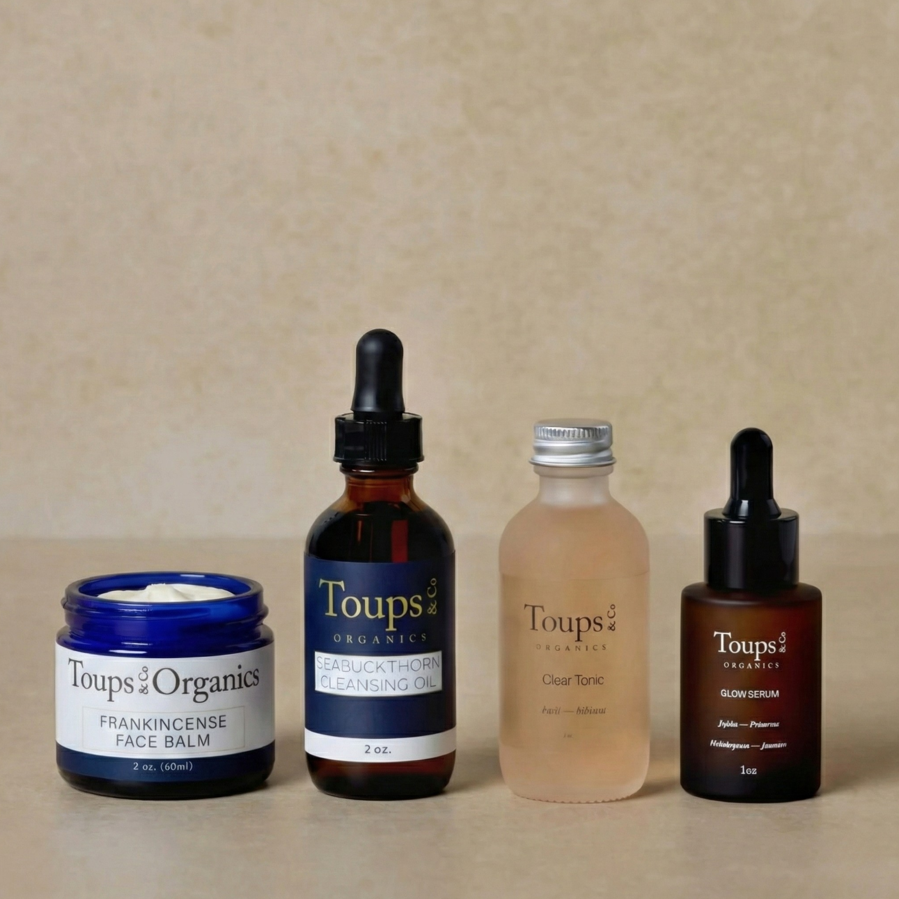 Toups and Co Organics’ Skincare Starter Set—featuring face balm, cleansing oil, clear tonic, and glow serum—appears in a row against a neutral background, highlighting these nontoxic clean beauty essentials.
