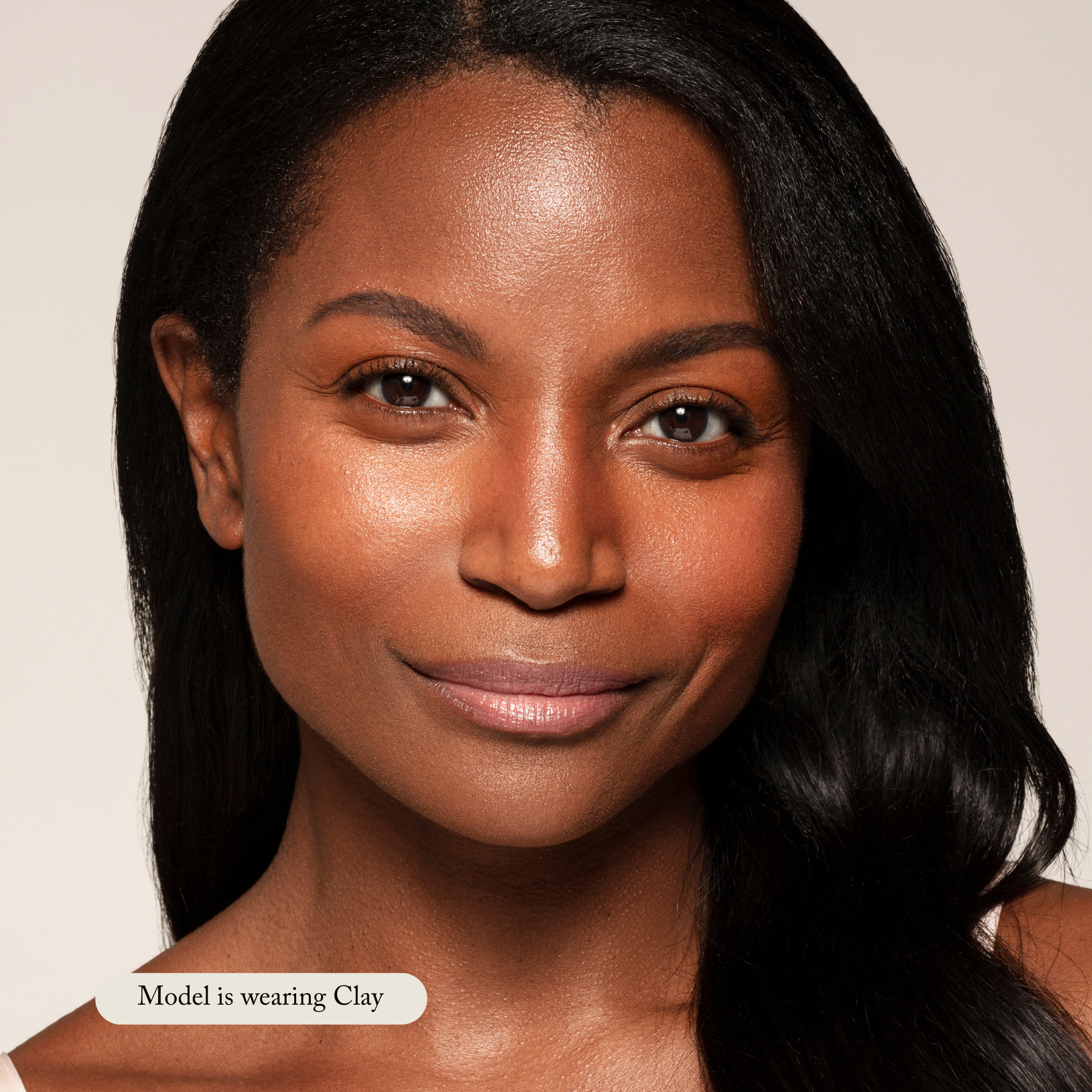 A woman with smooth, medium-brown skin and straight, dark hair smiles softly at the camera. Text reads: Model is wearing Toups and Co Organics Liquid Foundation in Clay for a natural glow.