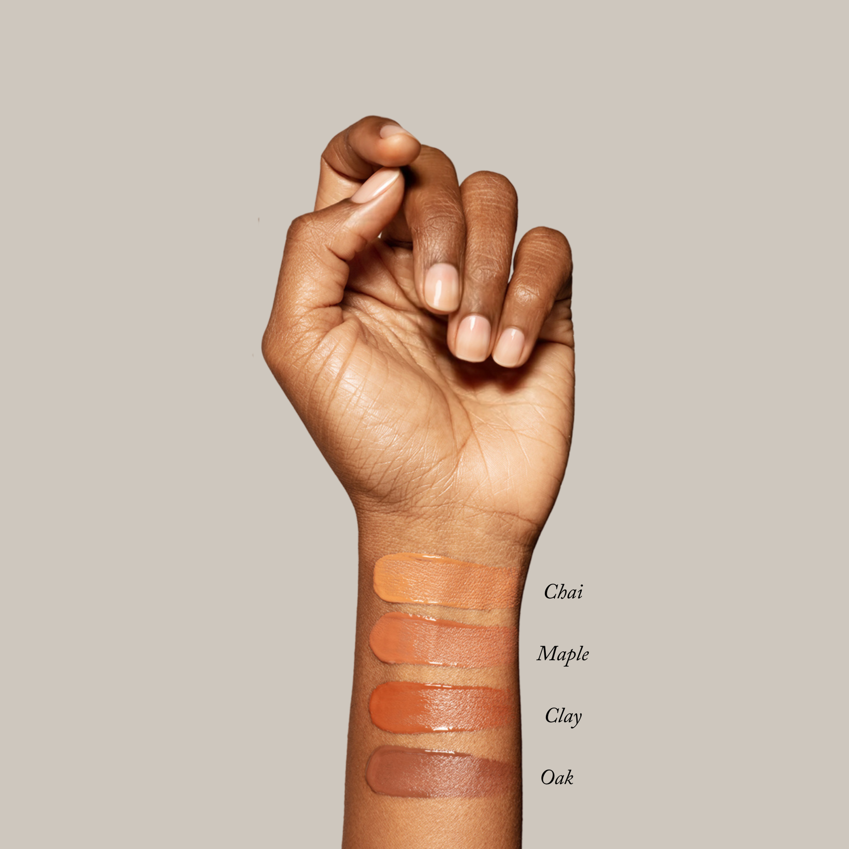 A hand displays four swatches of Toups and Co Organics Liquid Foundation in Chai, Maple, Clay, and Oak on the forearm against a neutral background—ideal for sensitive skin and achieving a natural glow.