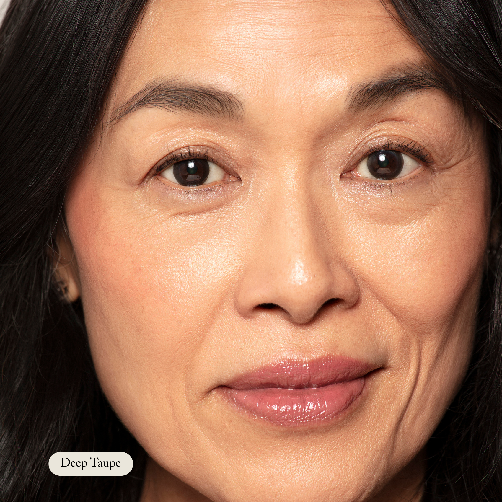Close-up of a woman with smooth skin, natural makeup, and glossy lips. The text “Deep Taupe” highlights Toups and Co Organics Brow Pencil, known for its buttery smooth application.