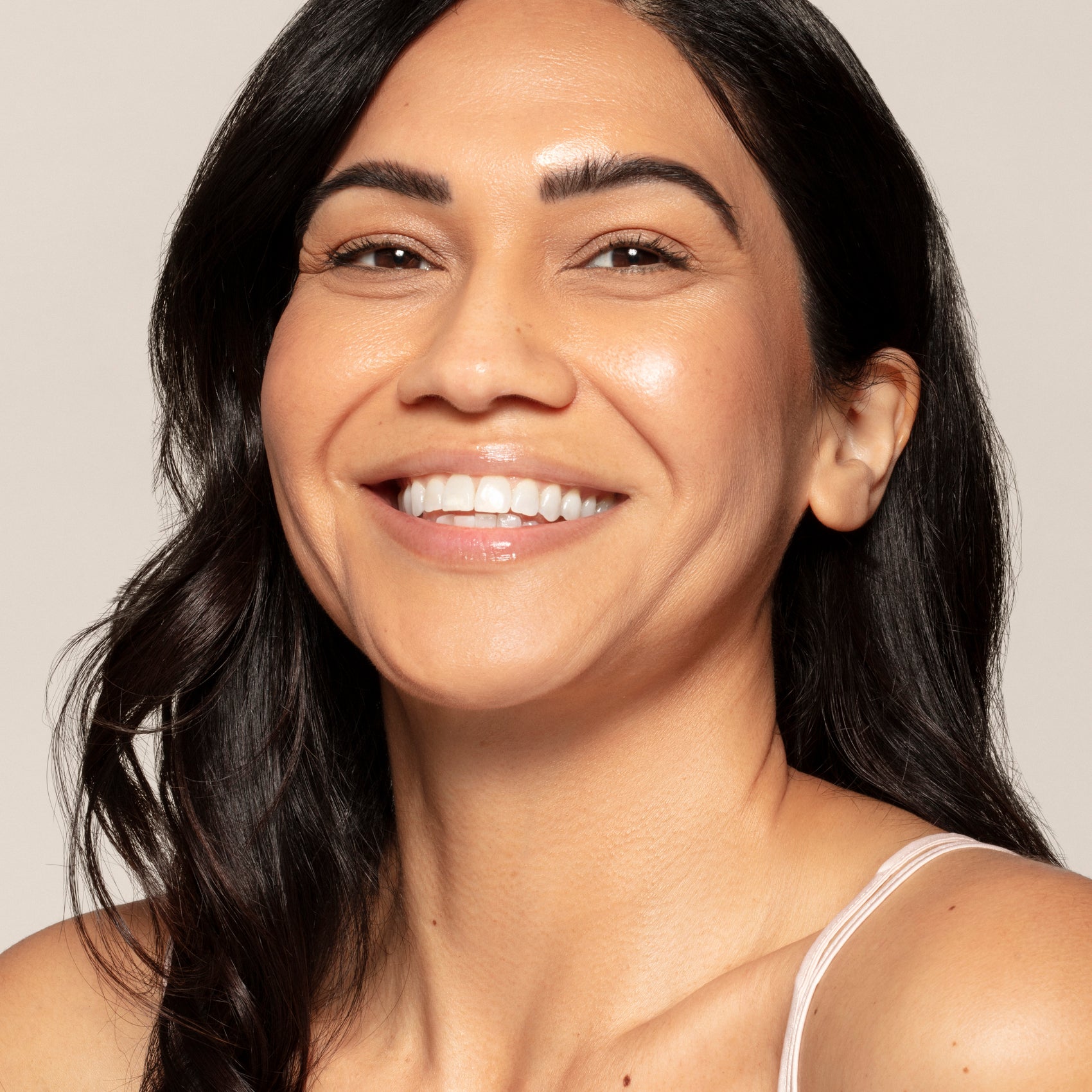 A woman with long dark hair and clear skin wears Toups and Co Organics Cream Luminizer Pot, smiling at the camera against a neutral background.