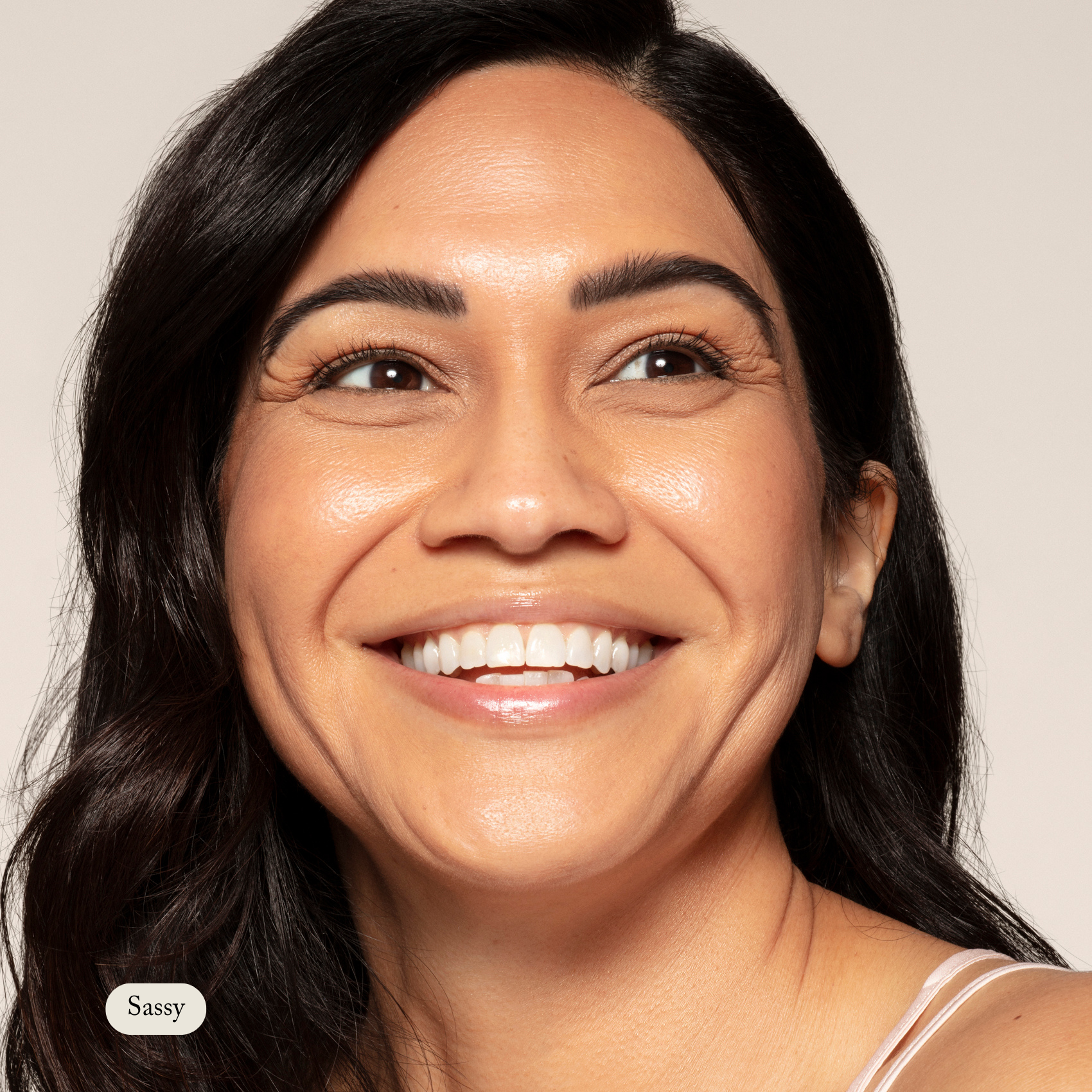 A woman with long dark hair smiles, revealing her glowing, hydrated skin—ideal for sensitive skin—while looking upward. In the bottom left, Sassy appears beside Toups and Co Organics Concealer.