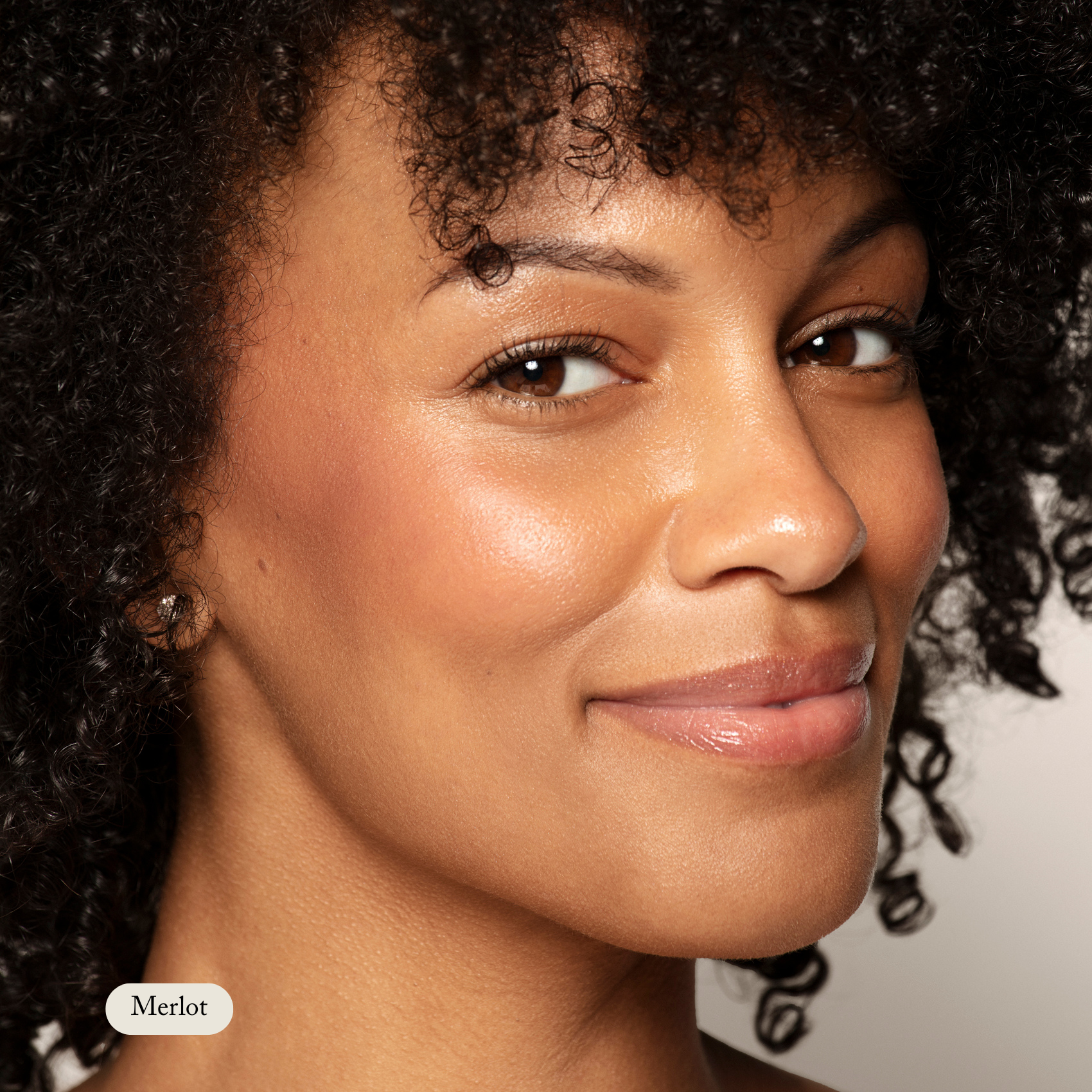 A woman with curly hair and a natural glow smiles at the camera. In the corner, an image label reads Cream Cheek Tint by Toups and Co Organics.