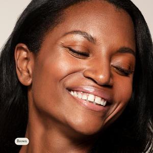 A woman with brown skin smiles with her eyes closed, highlighting Toups and Co Organics Natural Eyeliner—ideal for sensitive eyes—set against a neutral background.