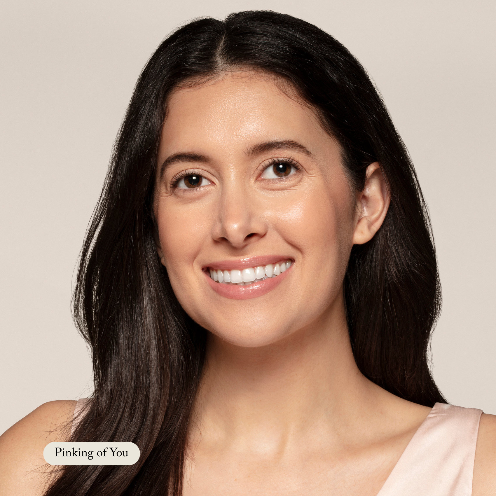 A woman with long dark hair in a light pink top smiles at the camera against a neutral background. A label reads: Toups and Co Organics—Organic Lip Gloss made with safe, nontoxic ingredients.
