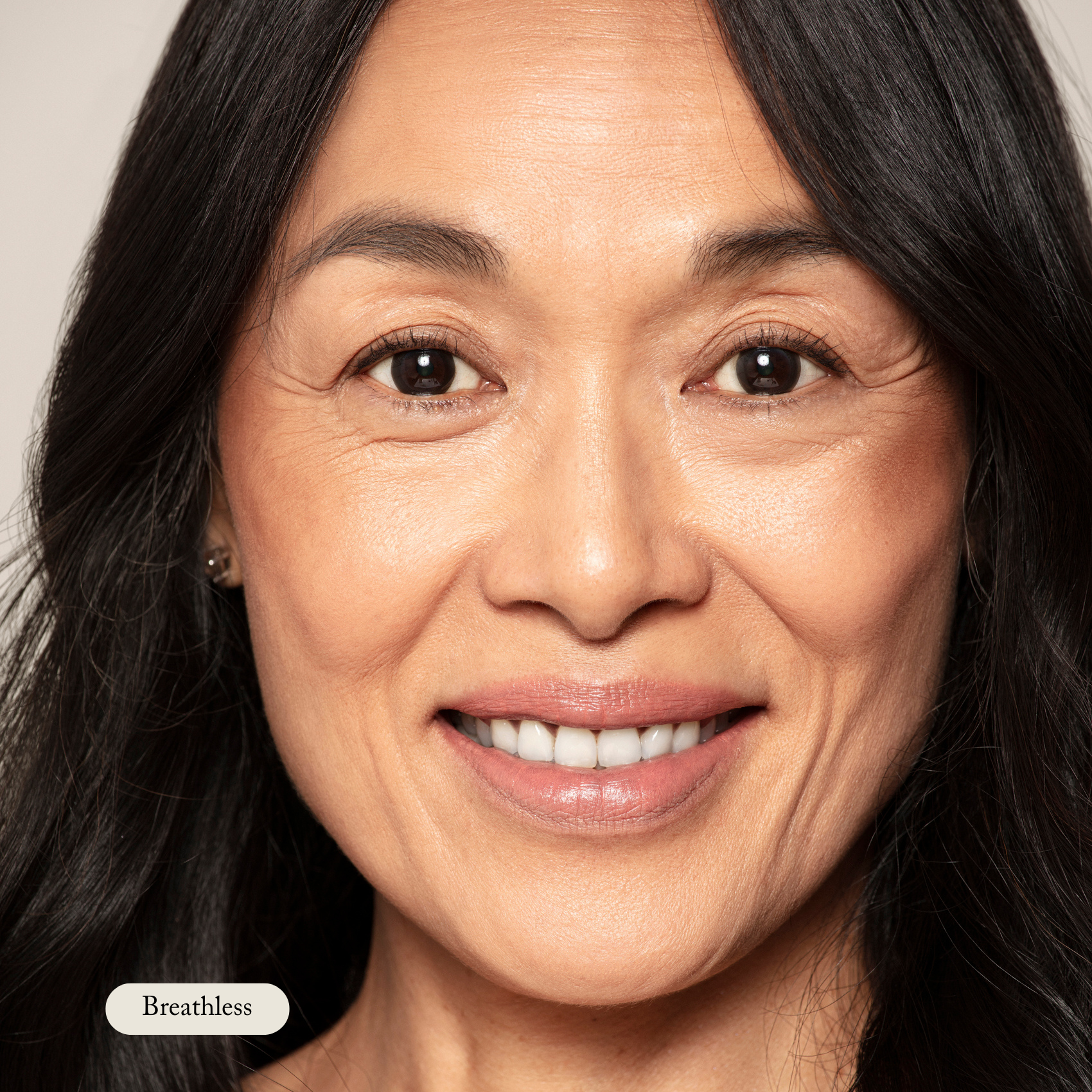 Close-up of a woman with long black hair softly smiling at the camera; “Breathless” appears in a label at the bottom left, showcasing Toups and Co Organics’ Nourishing Lipstick, infused with hydrating butters for smooth, soft lips.