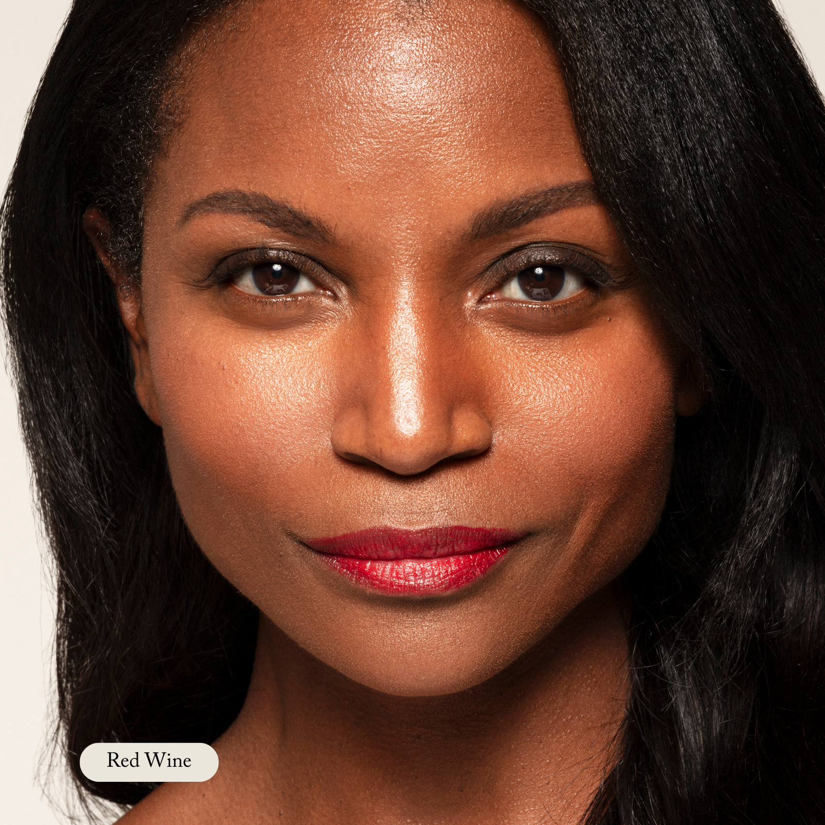 Close-up of a woman with long black hair, smooth skin, and lips in Red Wine shade. She wears Toups and Co Organics Nourishing Lipstick, enriched with antioxidants and hydrating butters, looking directly at the camera with a neutral expression.