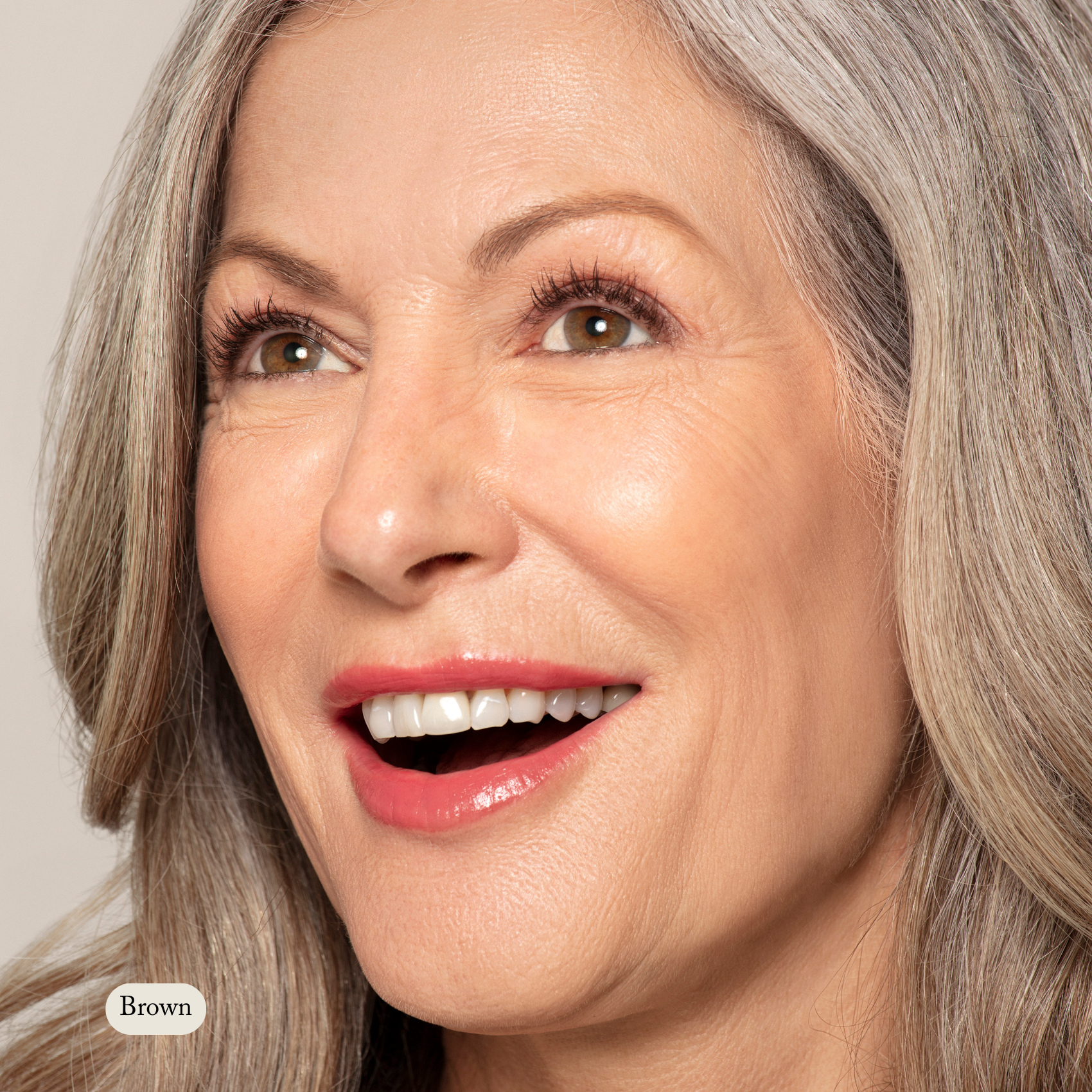 Close-up of a smiling older woman with long gray hair and brown eyes, wearing natural makeup enhanced by Toups and Co Organics Long Lash Mascara for fuller, healthier-looking lashes.