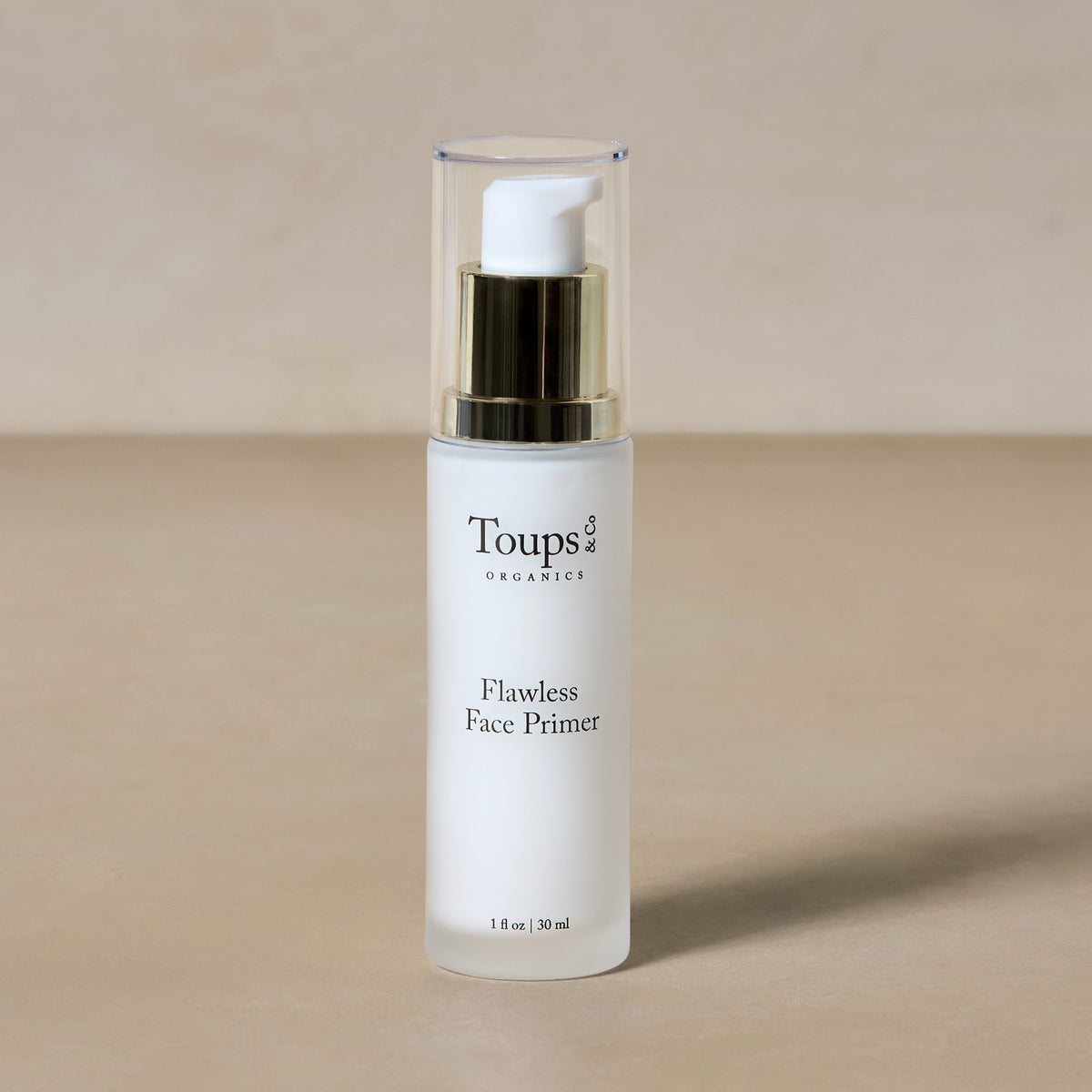 A bottle of Toups and Co Organics Flawless Face Primer with a pump dispenser rests on a neutral surface.
