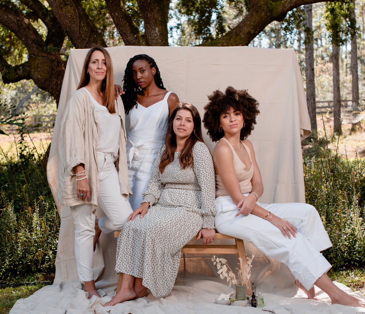 Four women posing outdoors in front of a draped linen backdrop.