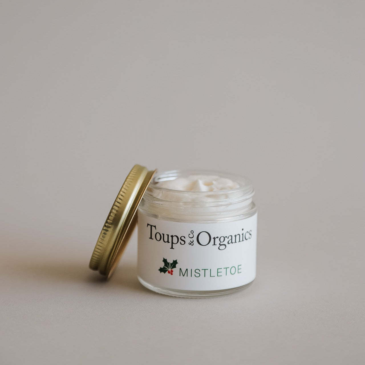A small glass jar of Toups and Co Organics Tallow Balm - Mistletoe with a gold lid, open against a neutral background—perfect as a unique Christmas gift.