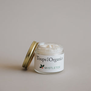 A small glass jar of Toups and Co Organics Tallow Balm - Mistletoe with a gold lid, open against a neutral background—perfect as a unique Christmas gift.