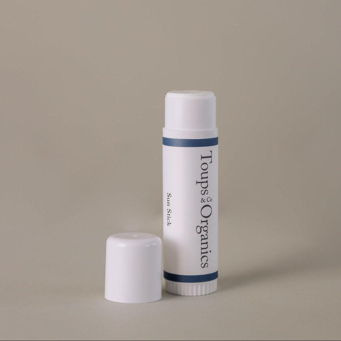 An upright white tube of the Toups and Co Organics Sun Stick is displayed with its cap beside it on a plain beige background, delivering effective sun protection and nourishing skincare.