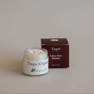 An open jar of Tallow Balm - Mistletoe by Toups and Co Organics, made with grass-fed tallow, sits by its maroon box—perfect for Christmas gifting.