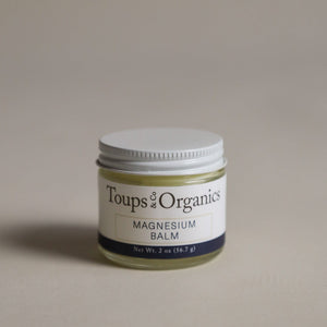 A small glass jar labeled "Magnesium Balm" from Toups and Co Organics with a white lid rests on a neutral background.