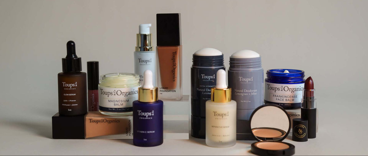 An assortment of Toups & Co. Organics skincare and makeup products, including serums, foundation, deodorant, magnesium balm, and lipstick.