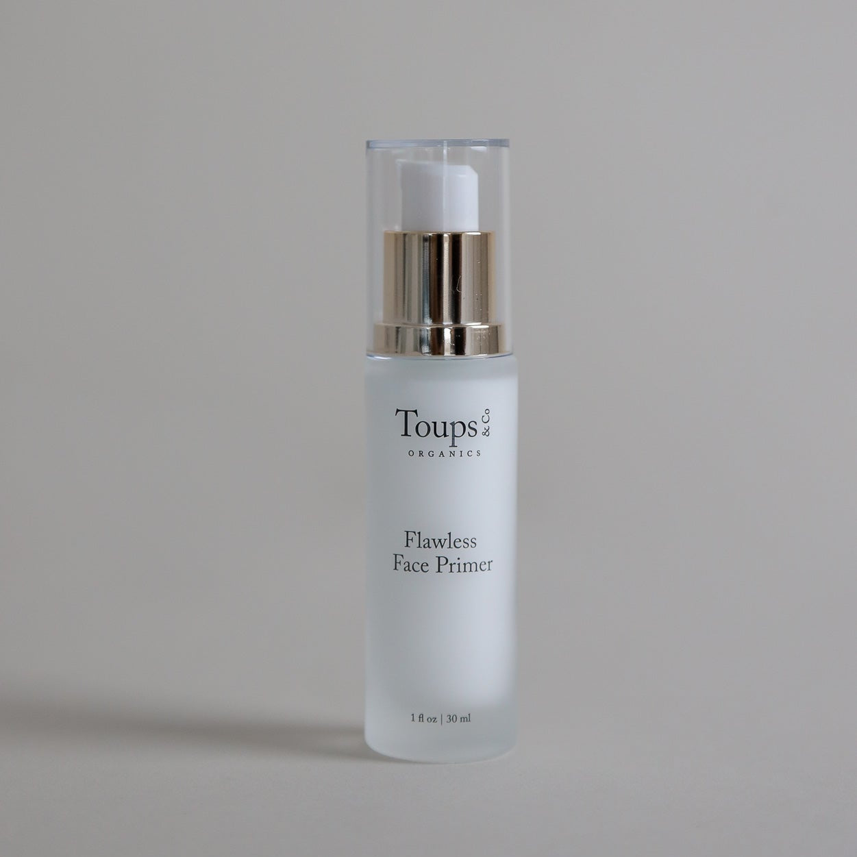 A bottle of Toups and Co Organics Flawless Face Primer with a pump dispenser rests on a neutral surface.