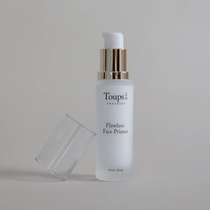 A bottle of Toups and Co Organics Flawless Face Primer with a pump dispenser rests on a neutral surface with the top off.