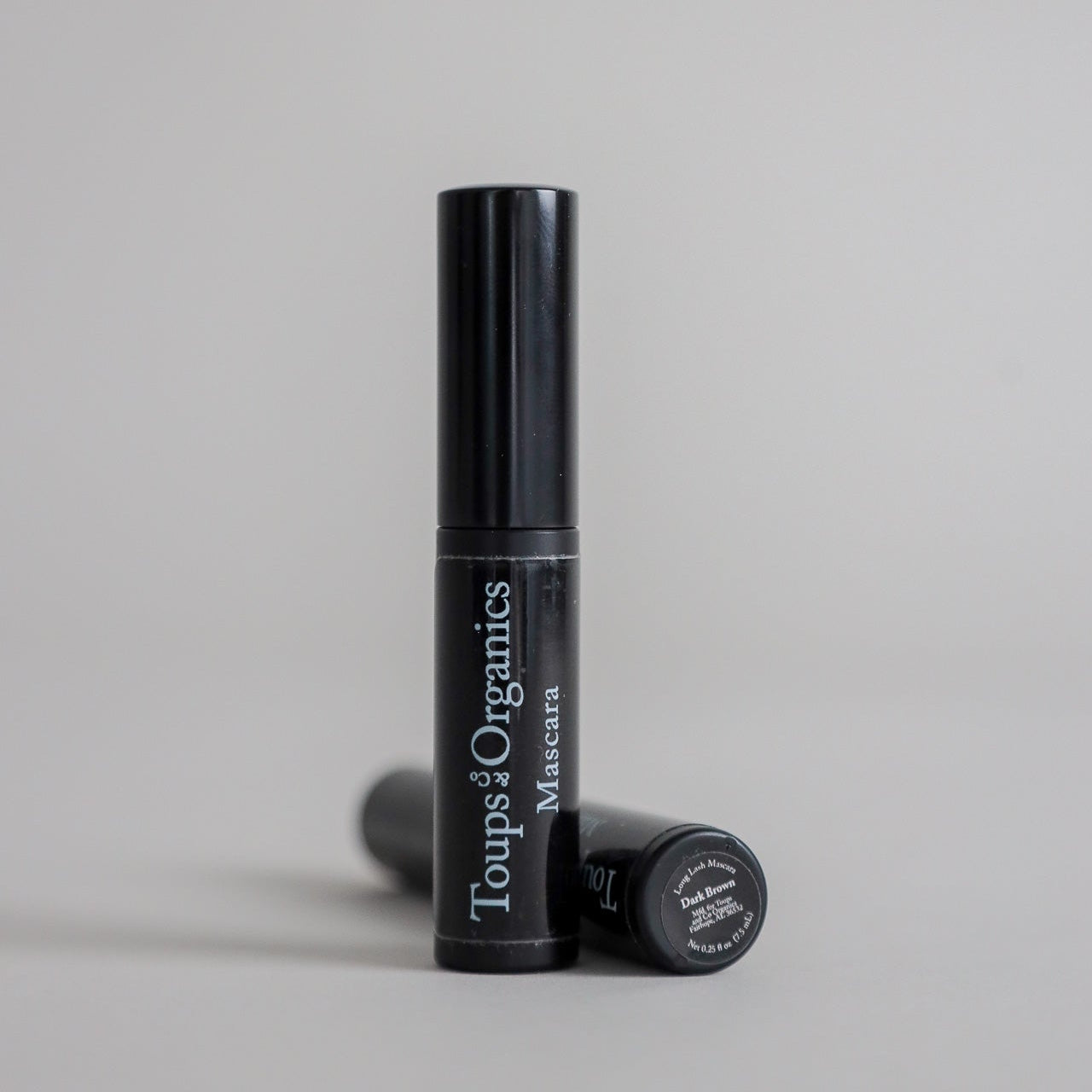 Product photography featuring two mascara tubes displayed on a clean grey seamless background, showcasing a sleek beauty cosmetic presentation.