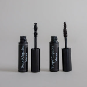 Product photography featuring two open mascara tubes with applicator brushes removed and displayed on a clean grey seamless background, highlighting the makeup product and mascara wands.