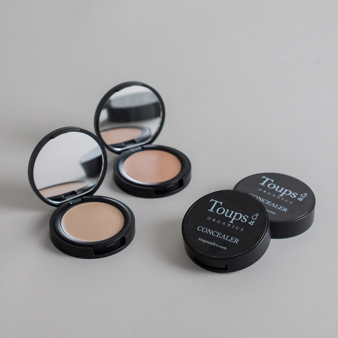 Toups & Co non-toxic concealers photographed open and closed on a soft grey seamless background, showcasing the creamy complexion product and sleek black packaging. Clean, minimalist product photography for natural makeup and everyday beauty.