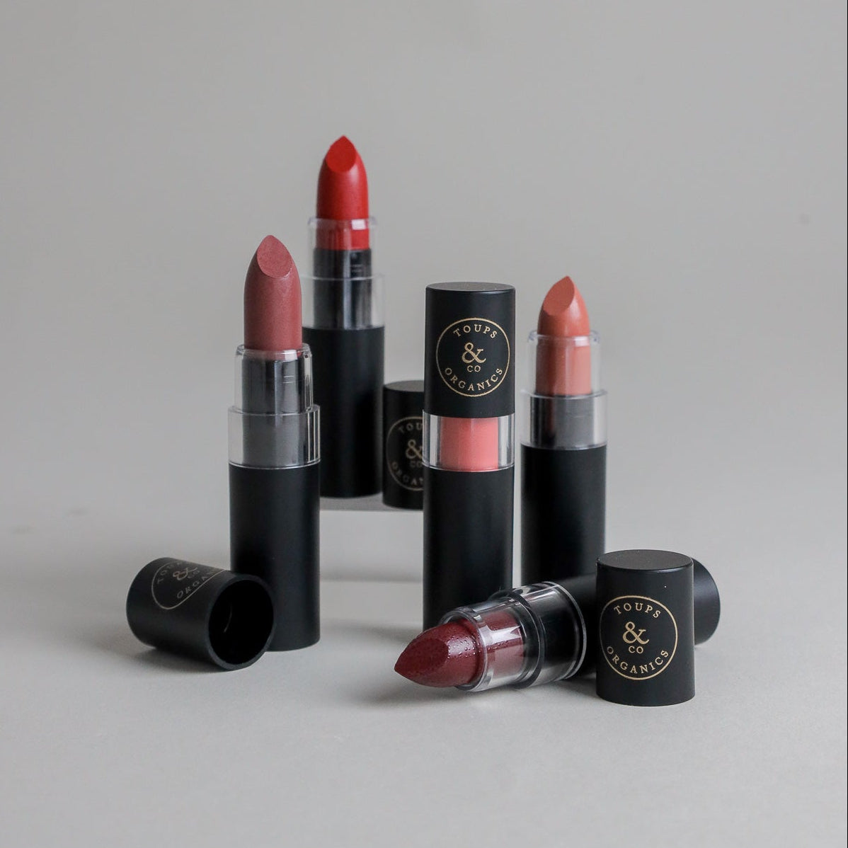 Toups & Co clean lipstick bullets in red, rose, and berry shades with caps removed