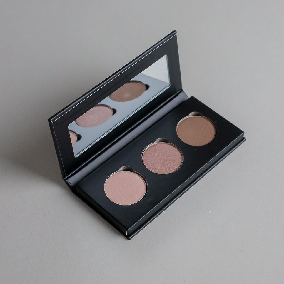 Close-up product photo of a three-shade eyeshadow palette displayed on a clean grey seamless background, showcasing versatile eyeshadow colors and a modern beauty aesthetic.