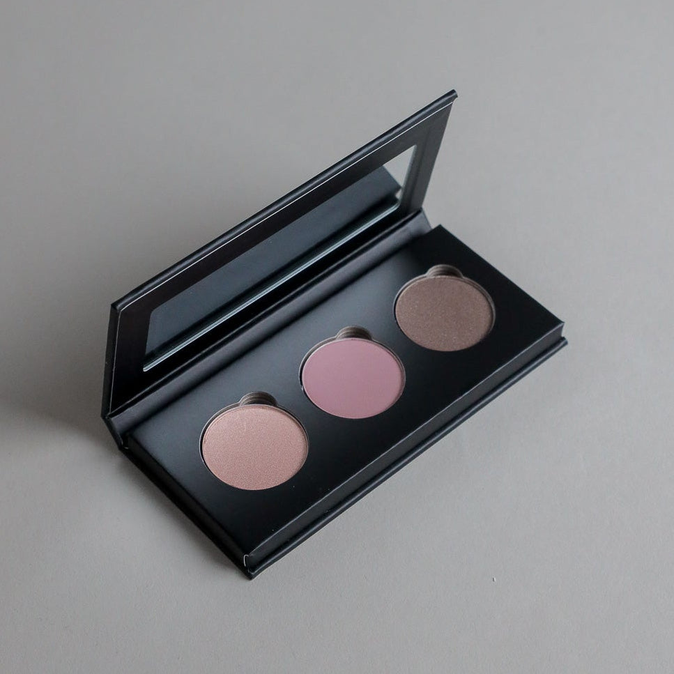 Close-up product photo of a three-shade eyeshadow palette displayed on a clean grey seamless background, showcasing versatile eyeshadow colors and a modern beauty aesthetic.