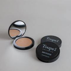 Toups & Co bronzer compacts photographed open and closed on a clean grey seamless background, showcasing the bronzer formula and classic black packaging. A minimalist beauty product image highlighting natural-looking complexion makeup.