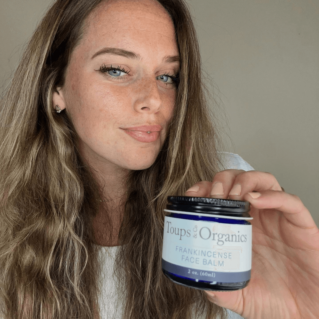 A woman holding a jar of Toups & Co Organics Frankincense Face Balm.