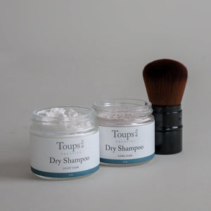 The Toups and Co Organics Clean Hair Set, featuring dry shampoo for both light and dark hair, is displayed beside a large makeup brush on a neutral background—ideal for oil-absorbing freshness and a gentle scalp detox.