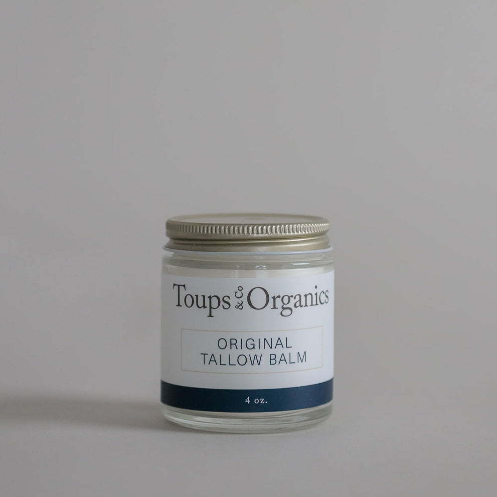 A glass jar labeled Tallow Balm - Original by Toups and Co Organics, 4 oz, offers whole-body moisture for dry, sensitive skin on a plain gray background.