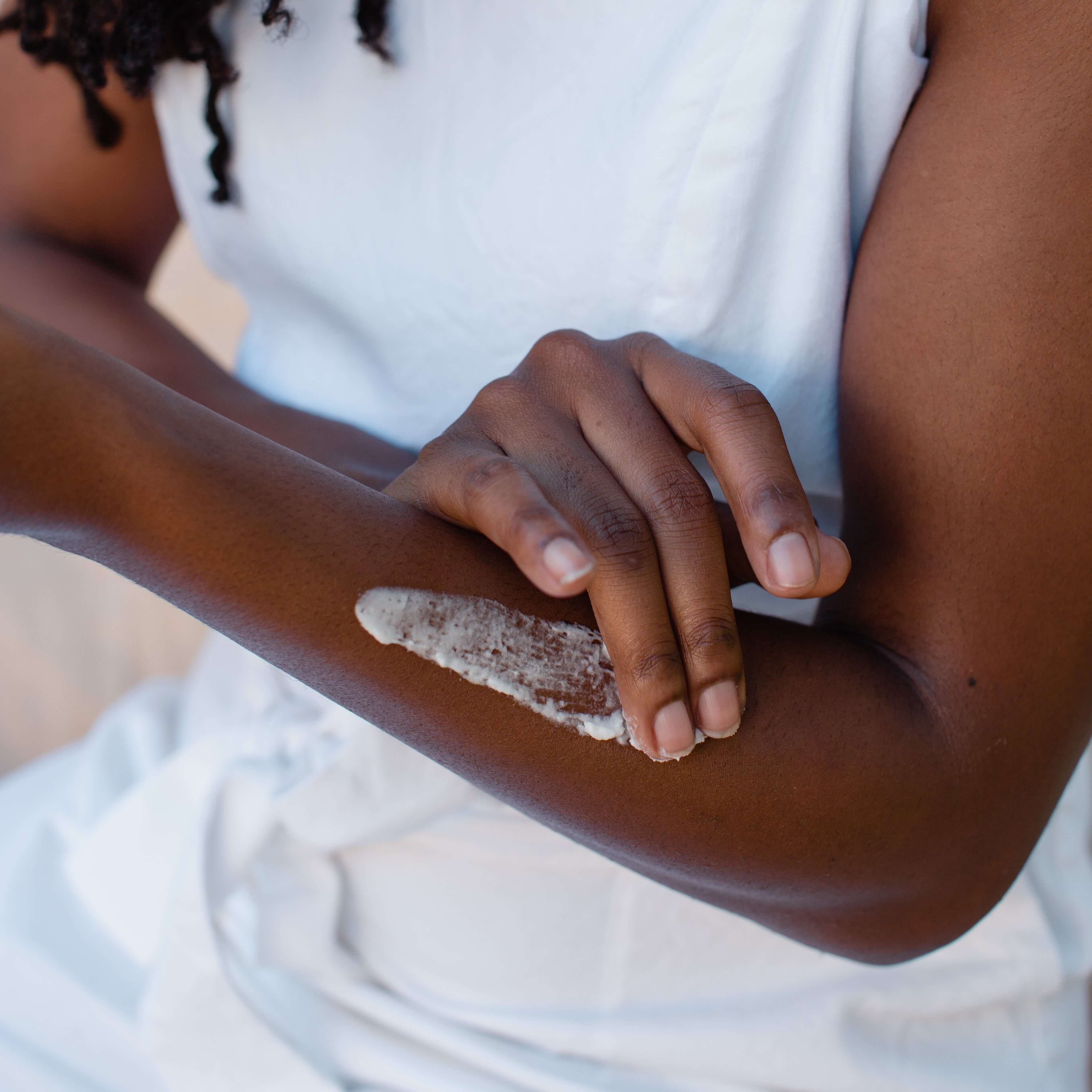 Wearing a white sleeveless top, a person applies Toups and Co Organics Tallow Balm - Original to their forearm for all-over hydration.