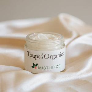 A jar of Toups and Co Organics Tallow Balm - Mistletoe, made with grass-fed tallow, rests on silky fabric—ideal for Christmas gifting.