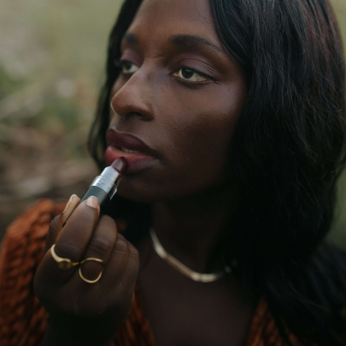 woman-applies-nontoxic-hydrating-lipstick-against-a-nature-background
